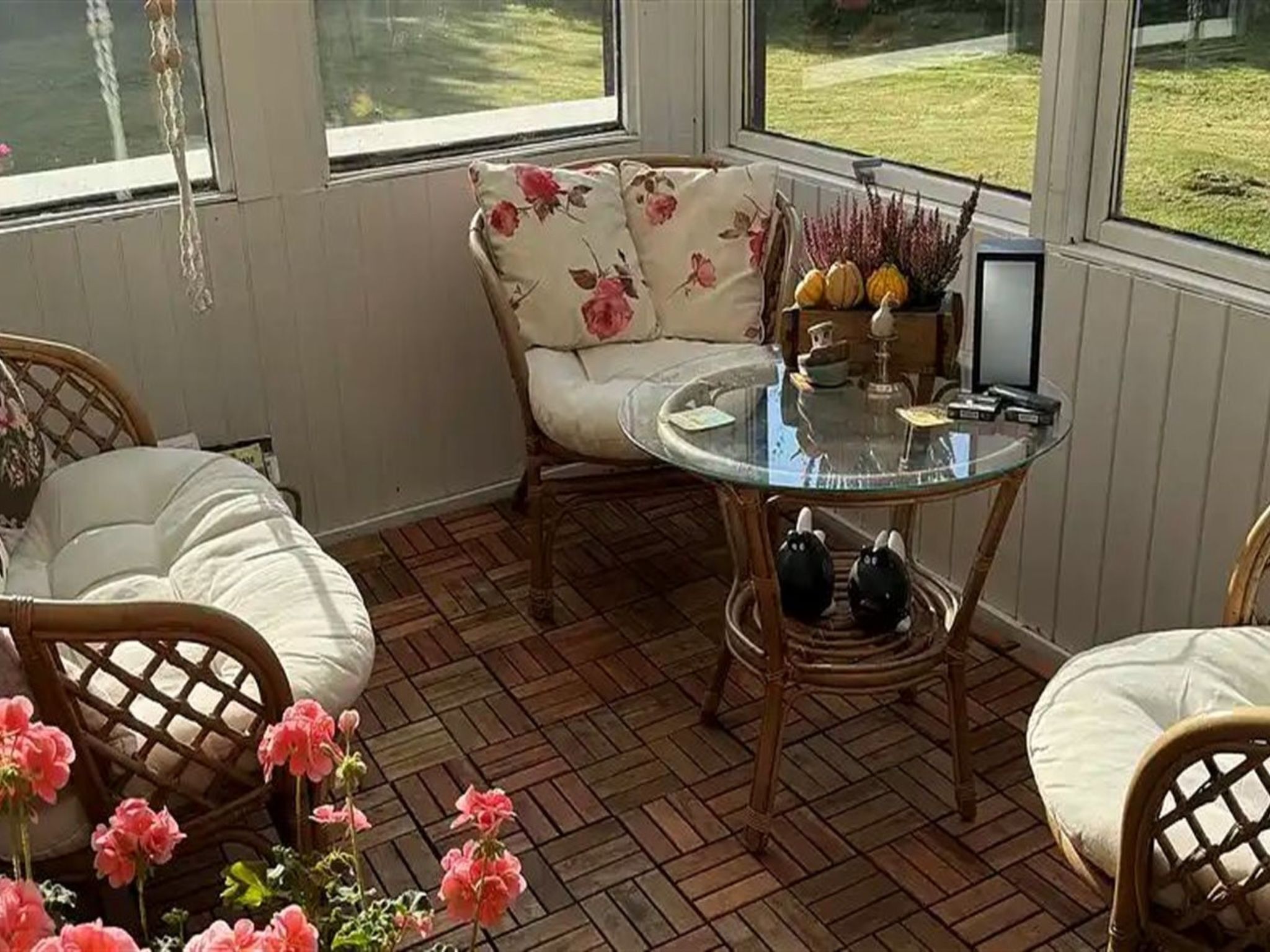 Une pièce baignée de lumière, avec une table ronde en verre, des meubles en osier et une vue sur une cour verdoyante grâce à de grandes fenêtres.