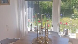 Ein Esstisch mit einer Tellerplatte mit Blumen, einem Kandelaber und Blick auf einen Garten durch ein Fenster.