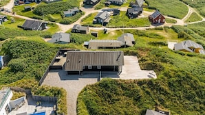 Vista aérea de uma área residencial com várias casas, um edifício central com telhado inclinado e uma piscina.