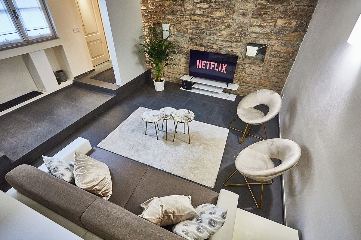 Een moderne woonkamer met een stenen muur, een flatscreen televisie, een potplant en een zithoek met een bank en twee fauteuils.