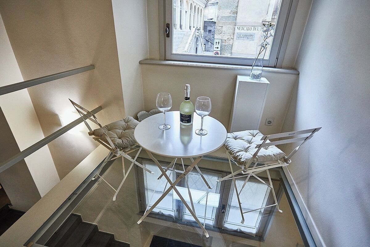 Un balcón con una mesa redonda, dos sillas, una botella de vino y dos copas.