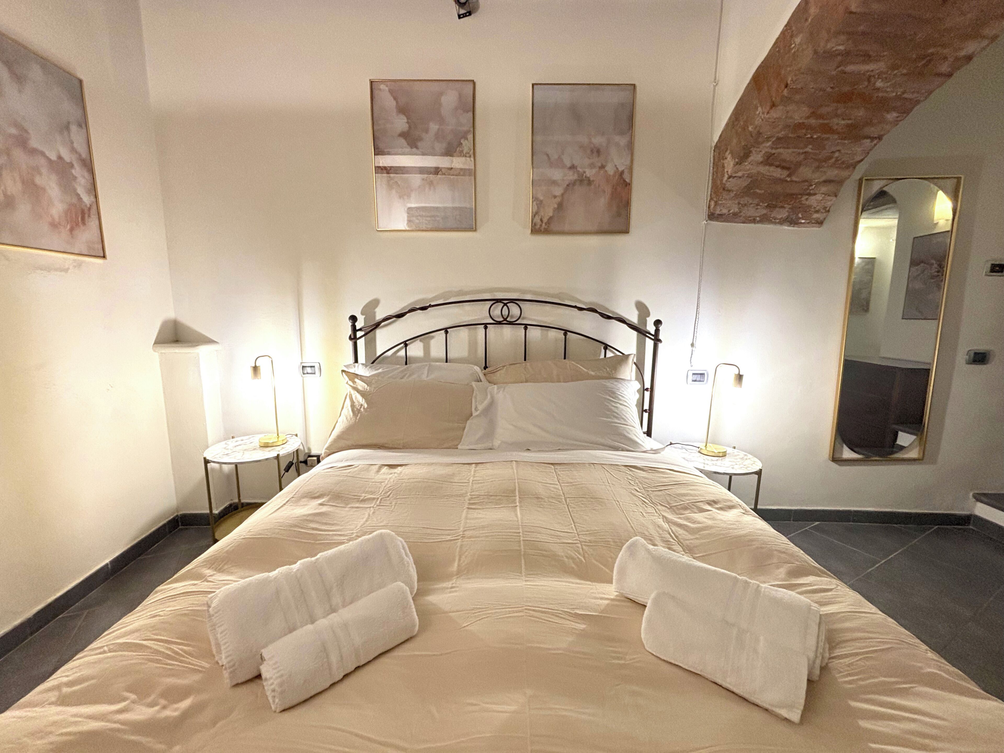 Ein ordentlich bezogenes Bett mit Kissen und Handtüchern, zwei Nachttische mit Lampen und ein großer Spiegel an der Wand.