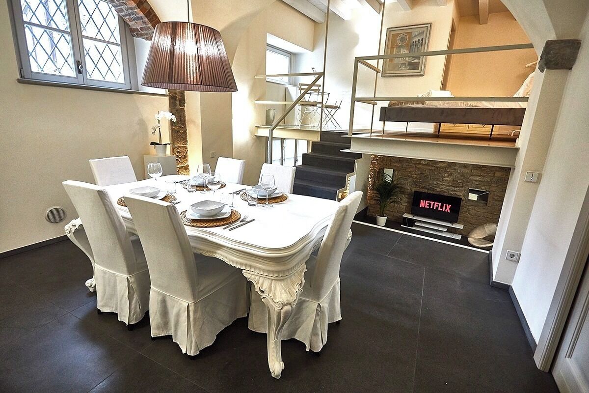 A dining area with a white table set for four, a fireplace with a Netflix sign, and a staircase leading to an upper level.