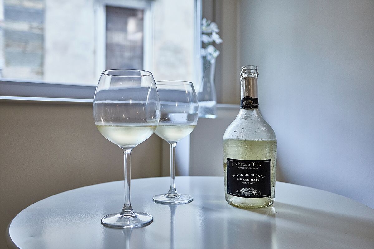 A bottle of Chateau Blanc Blanc de Blancs on a table with two empty glasses.