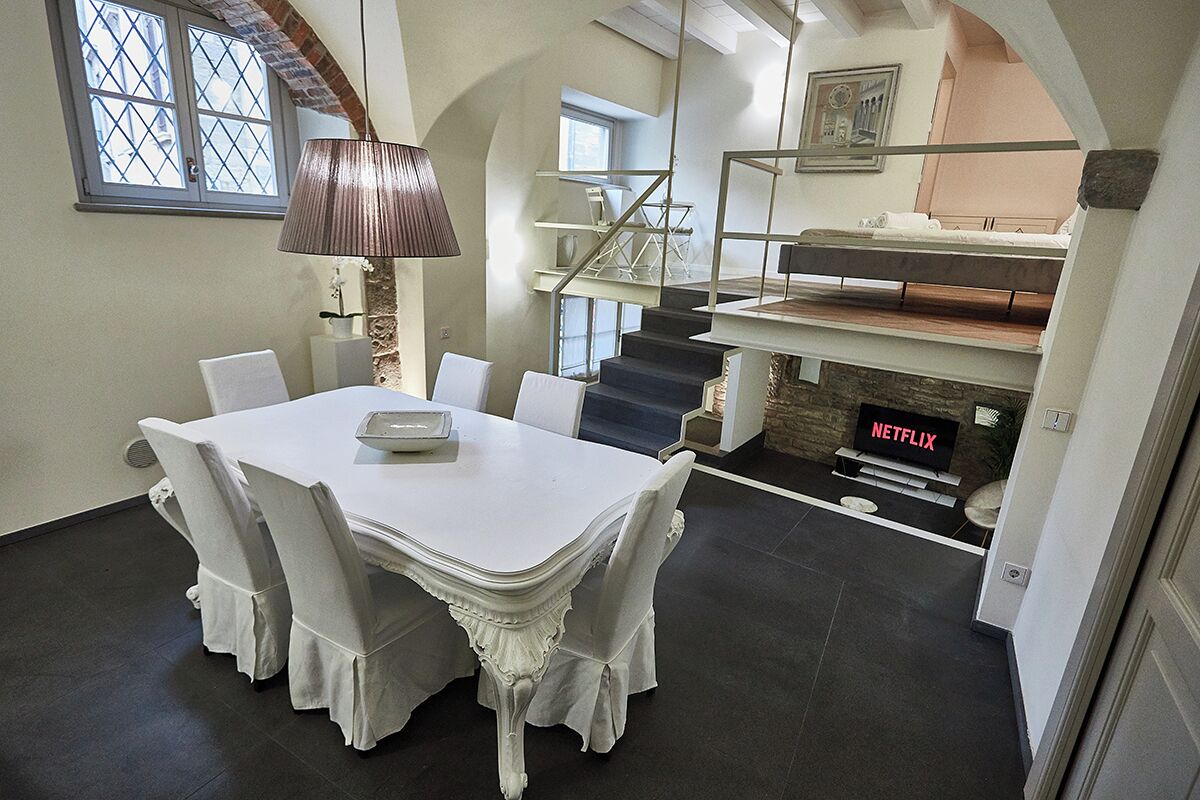 A dining area with a white table and chairs, a lamp, a staircase, and a TV displaying 'NETFLIX'.