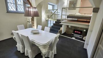 A dining area with a white table and chairs, a lamp, a staircase, and a TV displaying 'NETFLIX'.