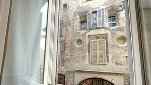 A view through a window of a building with multiple windows, some with shutters, and a circular window below. - Atlas Apartments - Città Alta (Bergamo)