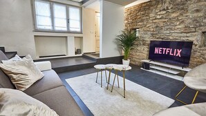 A modern living room with a stone wall, a large TV screen, a sofa, a coffee table, and a potted plant. - Atlas Apartments - Città Alta (Bergamo)