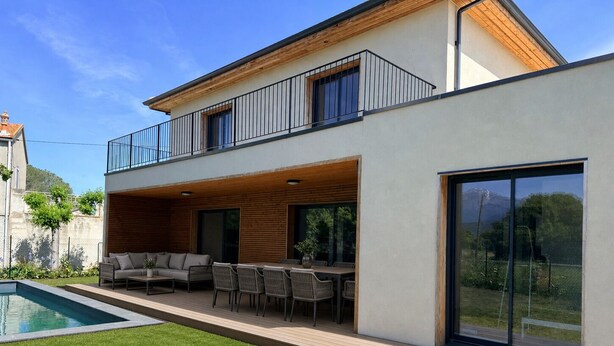Ein modernes, zweistöckiges Haus mit Pool, Sitzgelegenheiten im Freien und großen Fenstern.