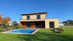 Ein modernes, zweistöckiges Haus mit Swimmingpool, gepflegtem Rasen und blauem Himmel.