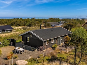 Ein modernes Haus mit dunklem Dach, einer Terrasse mit Gartenmöbeln und Blick auf die umliegende Landschaft.