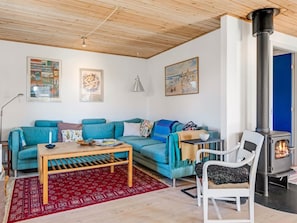 Ein gemütliches Wohnzimmer mit einem blauen Sofa, einem Holztisch, einem weißen Sessel und einem Kaminofen.