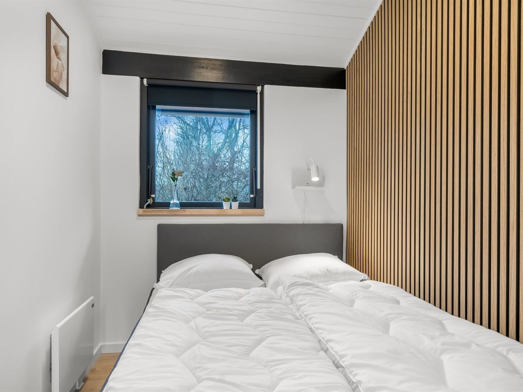 Et soveværelse med en seng, et vindue med udsigt til træer, en sengebordlampe og en radiator.