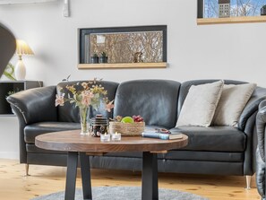 A modern living room with a dark leather sofa, a round wooden coffee table, and a vase with flowers. - "Gojko" -  from the sea by Interhome (Hals)