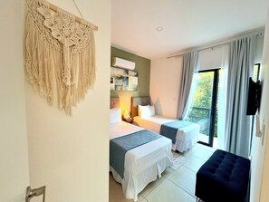 Ein Hotelzimmer mit zwei Betten, einem Fernseher, einem Balkon mit Vorhängen und einer Wanddekoration aus Makramee.