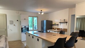 A modern kitchen with a central island, bar stools, a built-in oven, and a view of the outdoors. - Villa at the foot of Roussillon with private pool (Saint-Saturnin-lès-Apt)