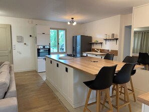 Une cuisine moderne dotée d’un îlot central, de tabourets de bar, d’un four encastré et offrant une vue sur l’extérieur.