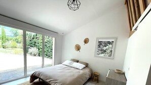 A modern bedroom with a bed, a small stool, a desk, and a window with a view of greenery. - Villa at the foot of Roussillon with private pool (Saint-Saturnin-lès-Apt)