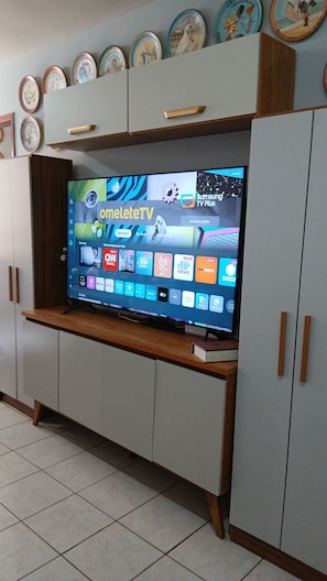 A flat-screen TV on a wooden stand in a room with a tiled floor and light-colored walls. -  Excelente Apartamento de 4 quartos no Buritis, em excelente localização (Belo Horizonte)