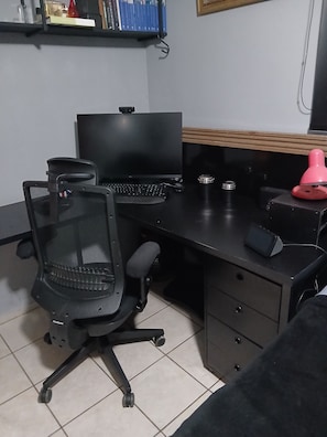 A workspace with a desk, chair, computer, and a shelf with books. -  Excelente Apartamento de 4 quartos no Buritis, em excelente localização (Belo Horizonte)