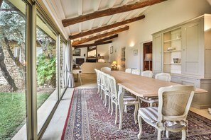 A dining area with a long table and chairs, a patterned rug, and a view of the outdoors. - Luxury and serenity, large private estate in Gordes. 5 air-conditioned rooms, (Gordes)