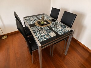 A dining table with a patterned tablecloth, four chairs, and a decorative centerpiece. - Pérola Apartments (Caniço)