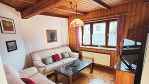 Une pièce chaleureuse avec des poutres apparentes, un canapé, une table et un téléviseur.
