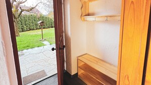 Une porte en bois qui donne sur une pièce où se trouvent un banc et une petite étagère.