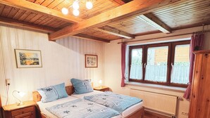 Une chambre à coucher en bois, avec un lit, des tables de chevet, une fenêtre avec des rideaux et un radiateur.