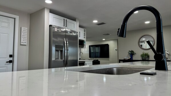 A modern kitchen with a stainless steel refrigerator, a black faucet, and a white countertop. - Lake house with kayaks, fishing & heated community pool (Holiday)