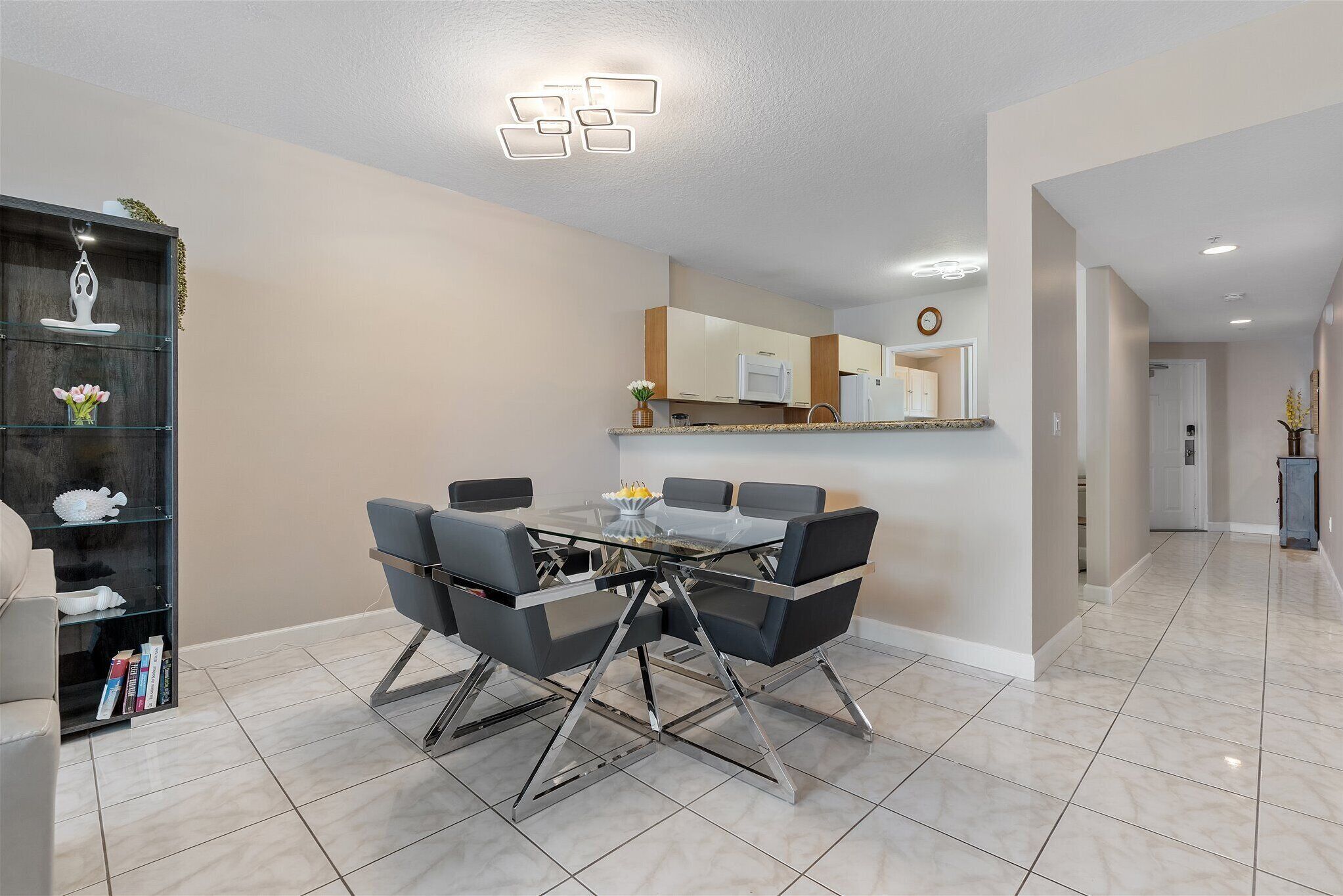 A modern dining area with a glass-top table, black chairs, and a kitchen in the background.