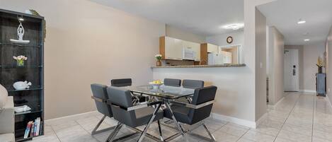 A modern dining area with a glass-top table, black chairs, and a kitchen in the background.