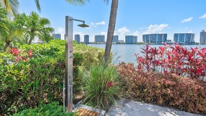 A waterfront view with dense foliage, a street lamp, and high-rise buildings in the background. - Spectacular Water Views 2br-4 beds in Sunny Isles Beach (Sunny Isles Beach)