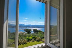 Vista a través de una ventana que muestra un lago, vegetación y montañas al fondo.
