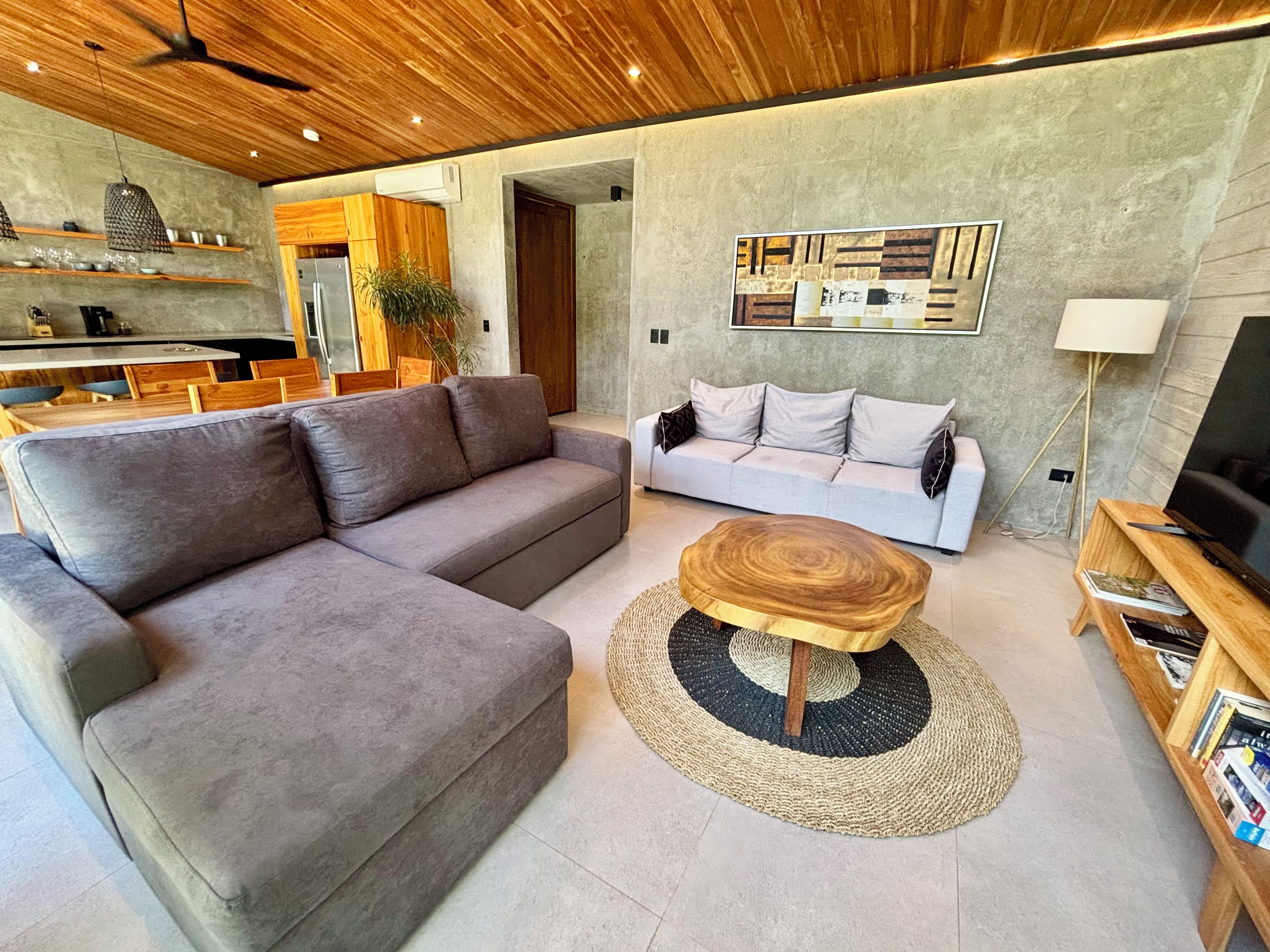 A modern living room with a grey sectional sofa, a round coffee table, and a white sofa with cushions.