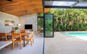 A modern interior with a dining area, a flat-screen TV, and a glass wall overlooking a pool and lush greenery. - Private Vacation Home in Tamarindo! Sleeps 6 (Tamarindo)