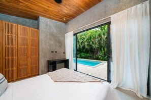 A bedroom with a large bed, a wooden wardrobe, a desk, and a view of a swimming pool through a glass door. - Private Vacation Home in Tamarindo! Sleeps 6 (Tamarindo)
