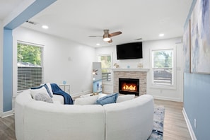 A living room with a fireplace, a ceiling fan, and a flat-screen TV mounted on the wall. - Stylish, Bright 3BR Retreat Near Downtown ATL (Atlanta)