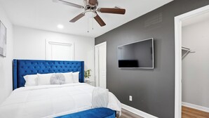 Una camera da letto con testiera trapuntata, TV a schermo piatto montata a parete, una panca e una ventola a soffitto.