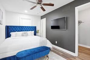 A bedroom with a tufted headboard, a flat-screen TV mounted on the wall, a bench, and a ceiling fan. - Stylish, Bright 3BR Retreat Near Downtown ATL (Atlanta)