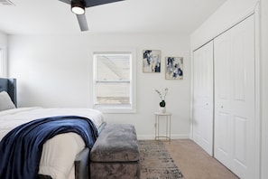 A bedroom with a bed, a bench, a small table with a plant, a window with blinds, and a closet. - Stylish, Bright 3BR Retreat Near Downtown ATL (Atlanta)