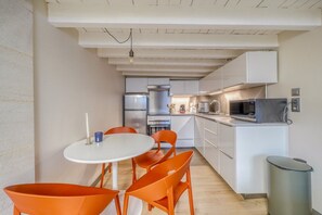 Eine kompakte Küche mit modernen Geräten, ein Essbereich mit orangefarbenen Stühlen und einem weißen Tisch.