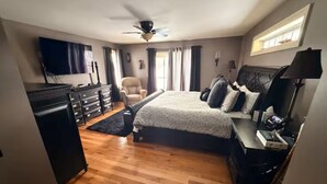 A bedroom with a bed, dresser, desk, chair, and a ceiling fan.