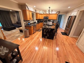 A modern kitchen with wooden cabinets, a central island, stainless steel appliances, and a dining area with a table and chairs. - Hiland Park Estate: Stunning Views & Large Ensuits (Queensbury)