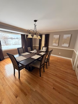 Un coin repas avec une table en bois foncé, six chaises et un lustre.