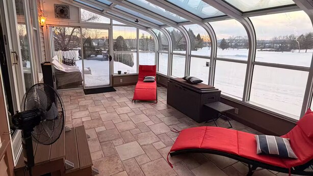 A covered outdoor area with a fan, red lounge chairs, and a view of a snowy landscape.