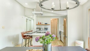 Uma cozinha moderna com uma ilha central, uma sala de jantar com mesa e cadeiras, e um lustre.