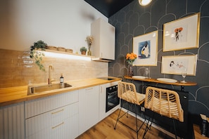 Ett modernt kök med en bänkskiva i trä, vita skåp och en inbyggd ugn. Det finns två fåtöljer i rotting och ett litet bord med en vas med blommor.