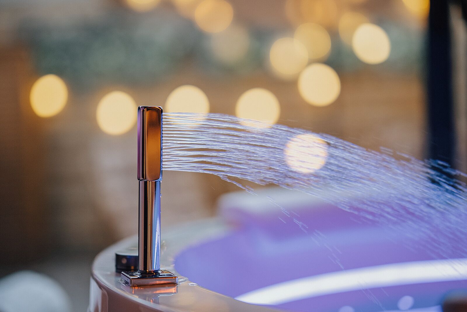 A water feature with a spout, a reflective surface, and a blurred background with lights.