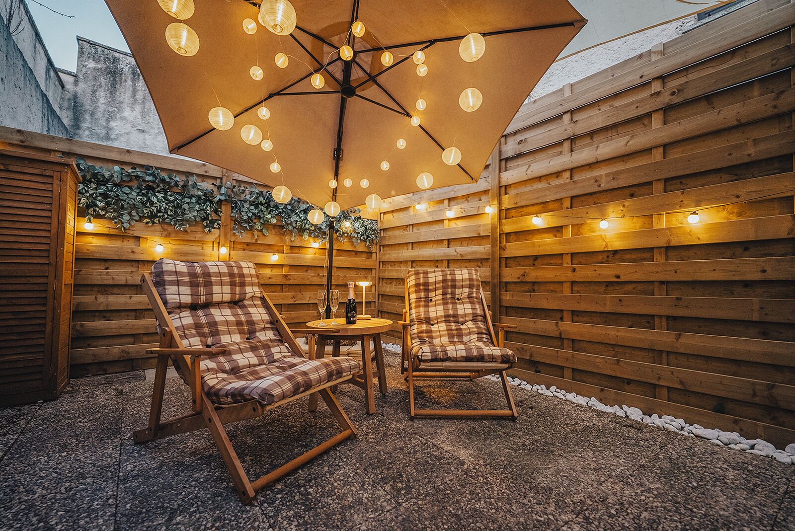 An outdoor patio with two plaid chairs, a round table, and a large umbrella.